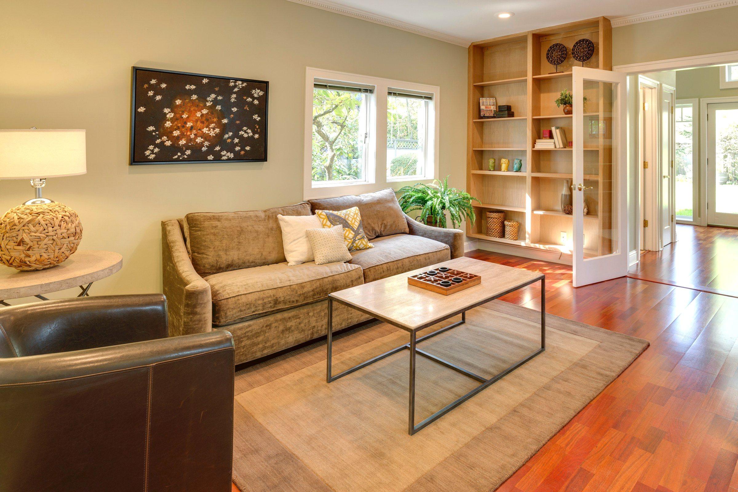 A bright, styled living room with warm wood floors, soft neutral furnishings, and natural light.